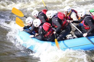 Group white water rafting on a Peak District river during an outdoor team experience.